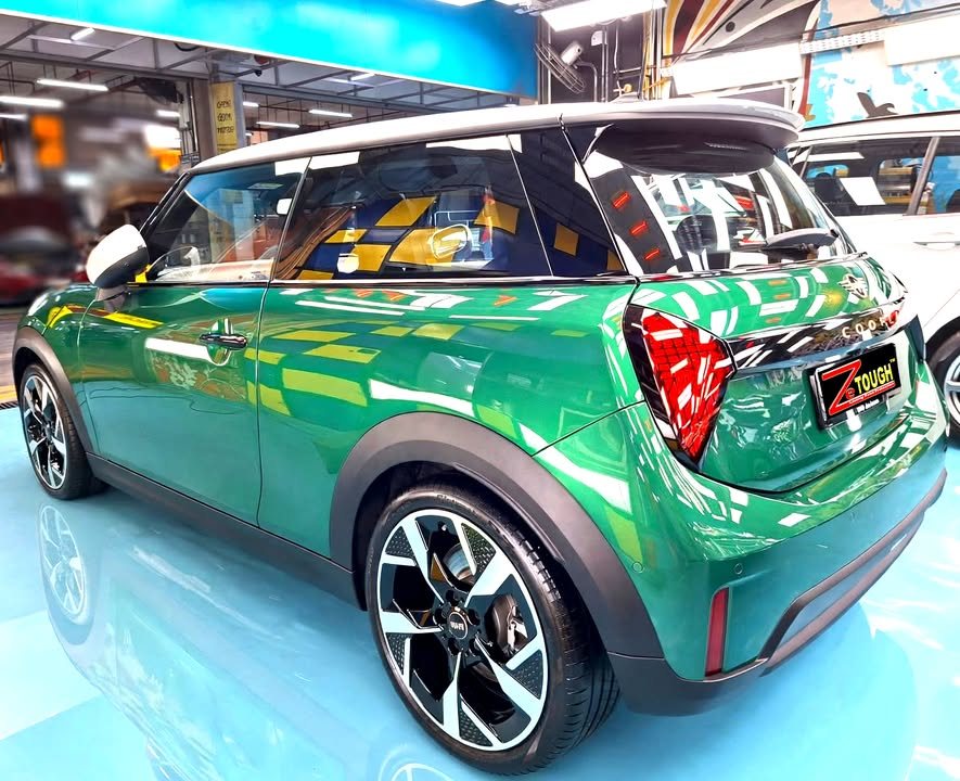 Rear three-quarter view of the green MINI Cooper with white roof in the workshop.