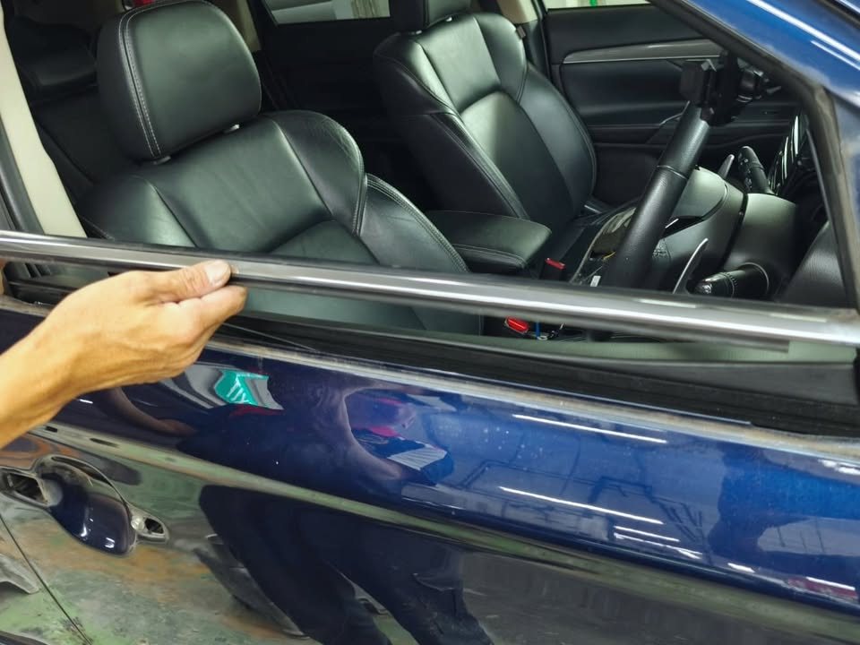 Hand lifting the window trim strip from the Outlander's door.
