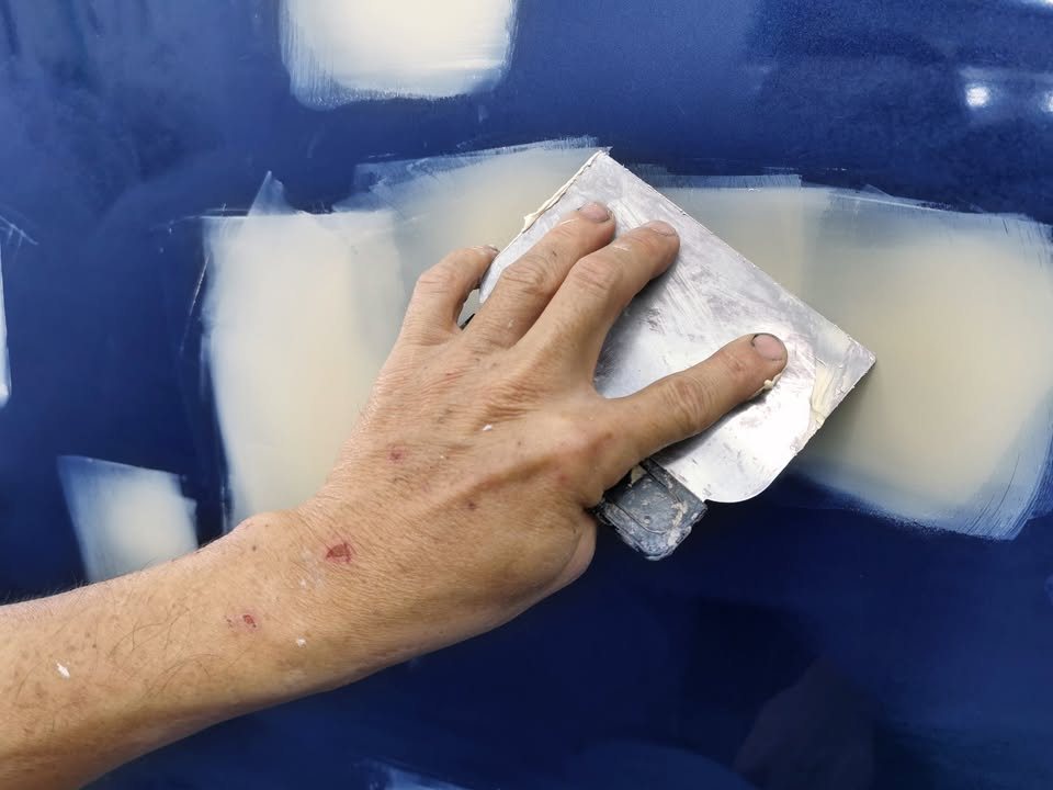 Hand spreading filler over patches on a dark blue panel.