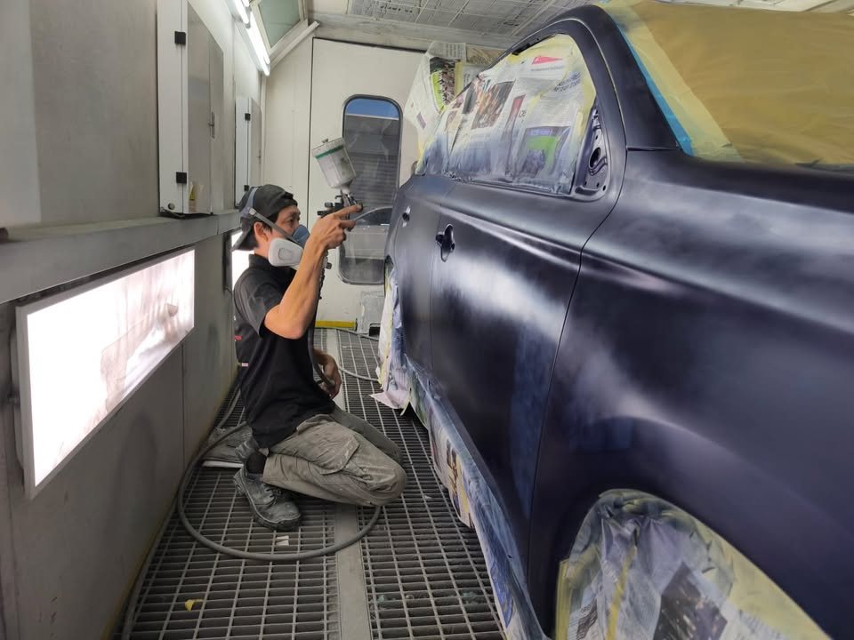 Painter in a mask spraying the side of the Outlander in the spray booth.