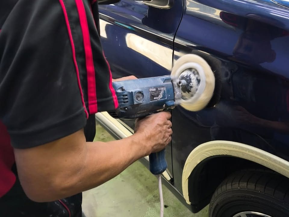 Team member machine polishing the newly painted dark blue door.