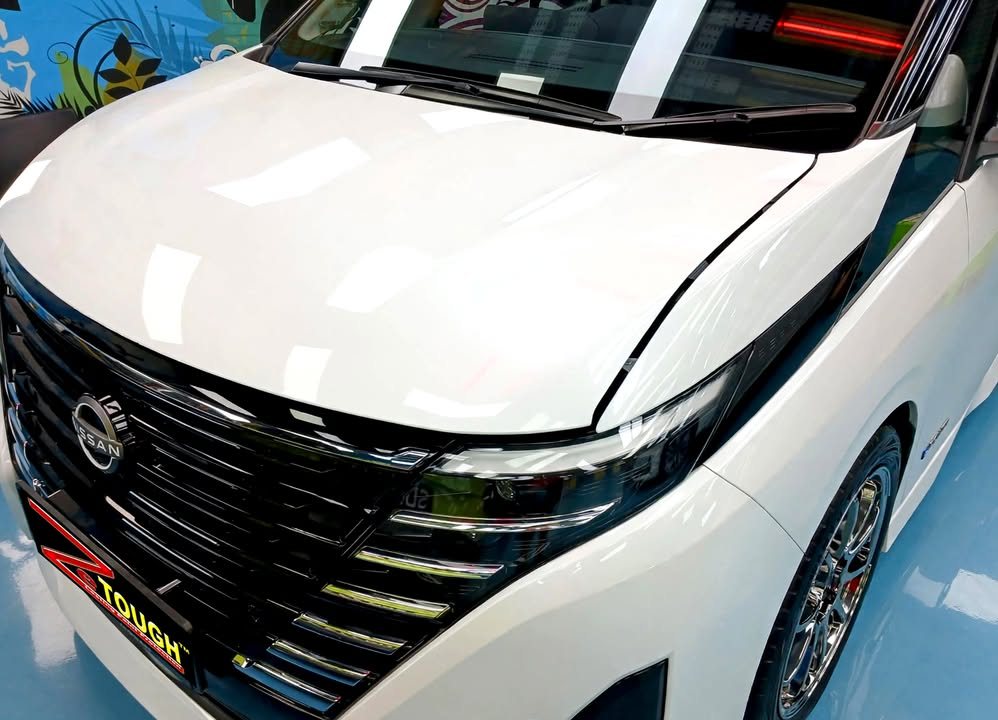 Close-up of the Serena's black grille and white bonnet reflecting the workshop lights.