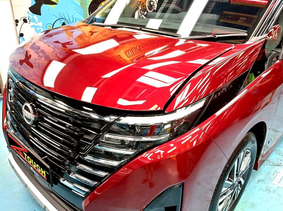 Front grille and bonnet of the red Serena with workshop lights reflected in the paint.