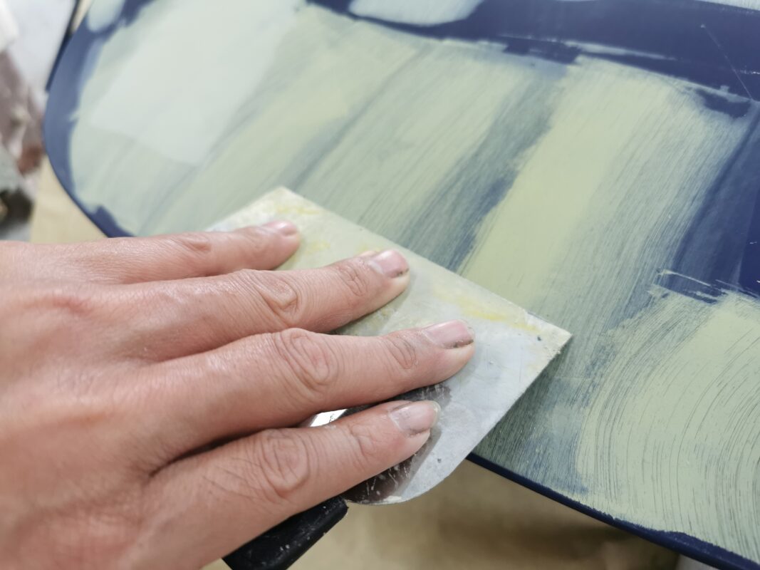 A technician applying body filler to a damaged panel on the 718 Cayman.