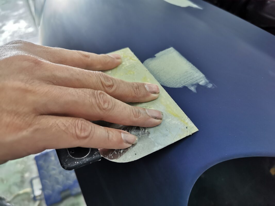 Surface inspection and patching on the Porsche 718 Cayman, every flaw marked for repair.