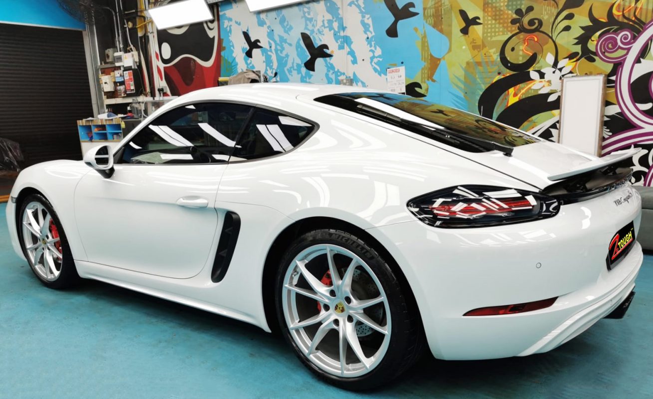 The coated bonnet of the Porsche 718 Cayman under workshop lighting.