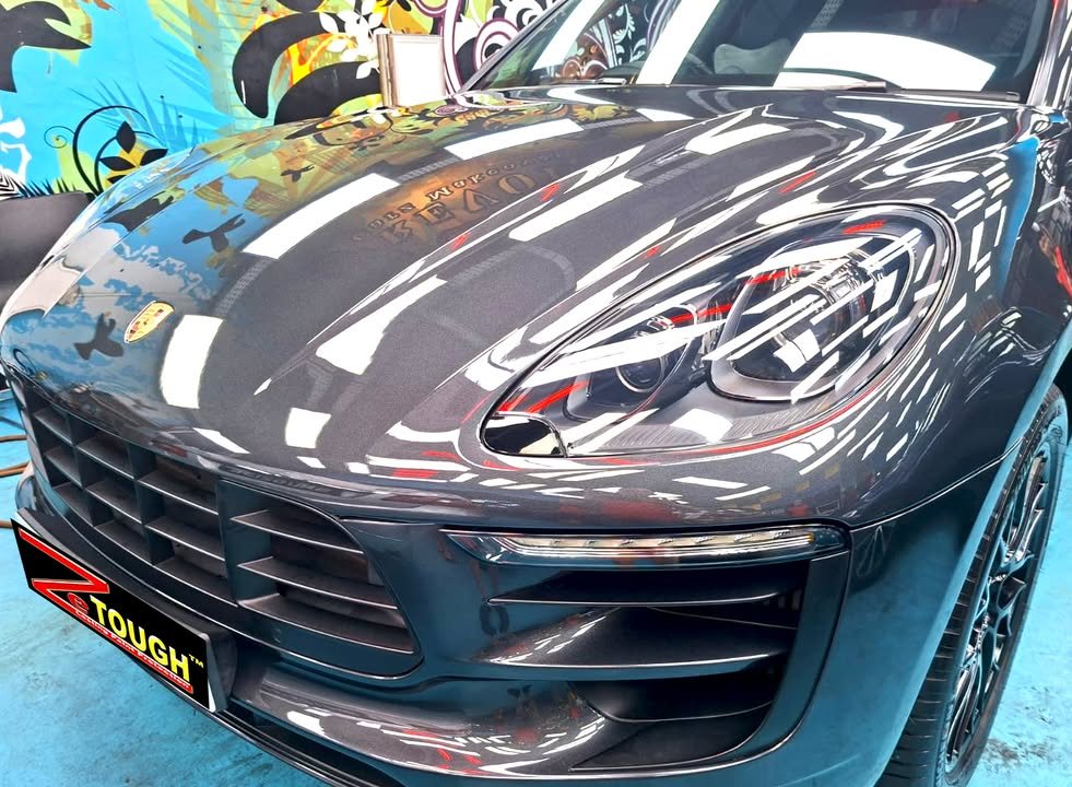 Dark grey bonnet and front bumper of the Porsche Macan reflecting the workshop lights.