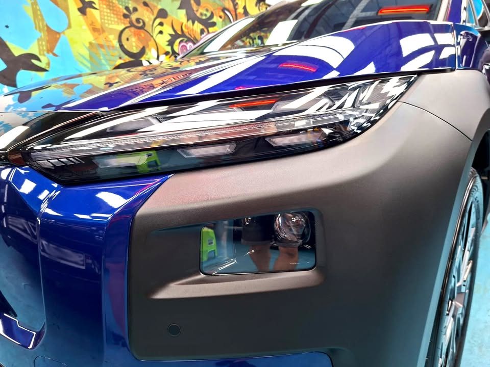 Close-up of the Subaru E-Outback headlight and front bumper, with lights reflected in the blue bonnet.