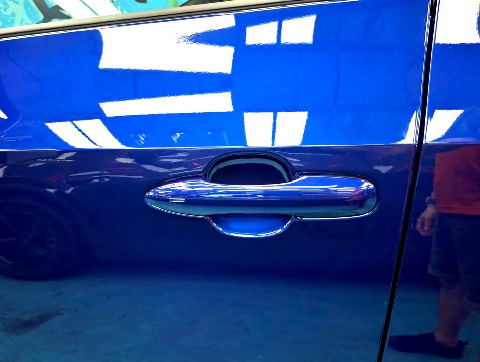 Close-up of the blue door panel and handle reflecting the workshop lights.