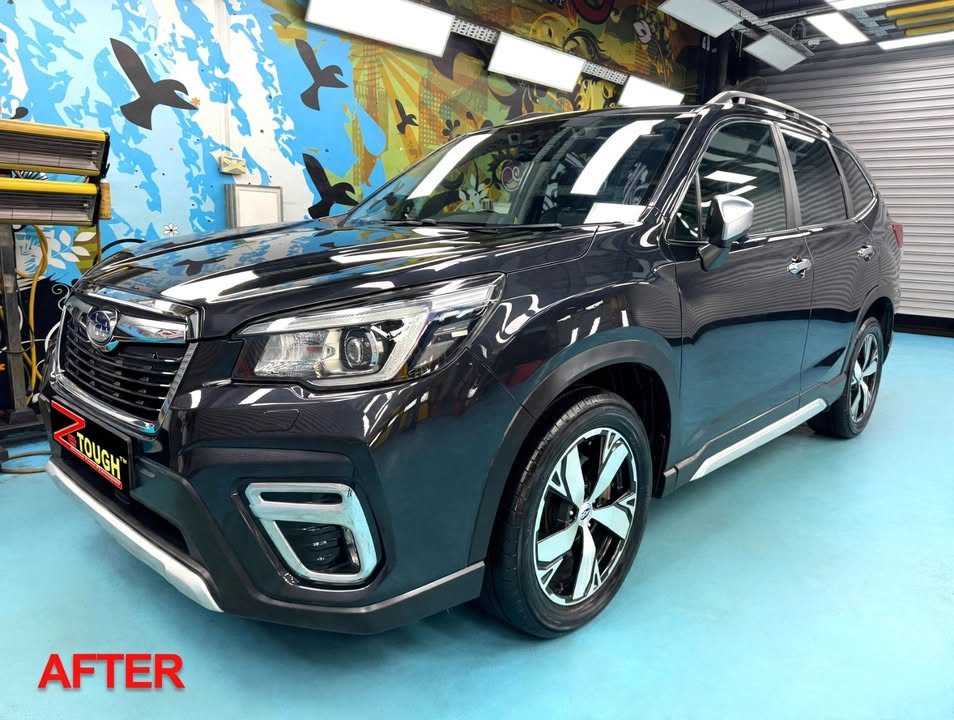 The finished dark grey Subaru Forester from the front three-quarter, glossy paint under the workshop lights.