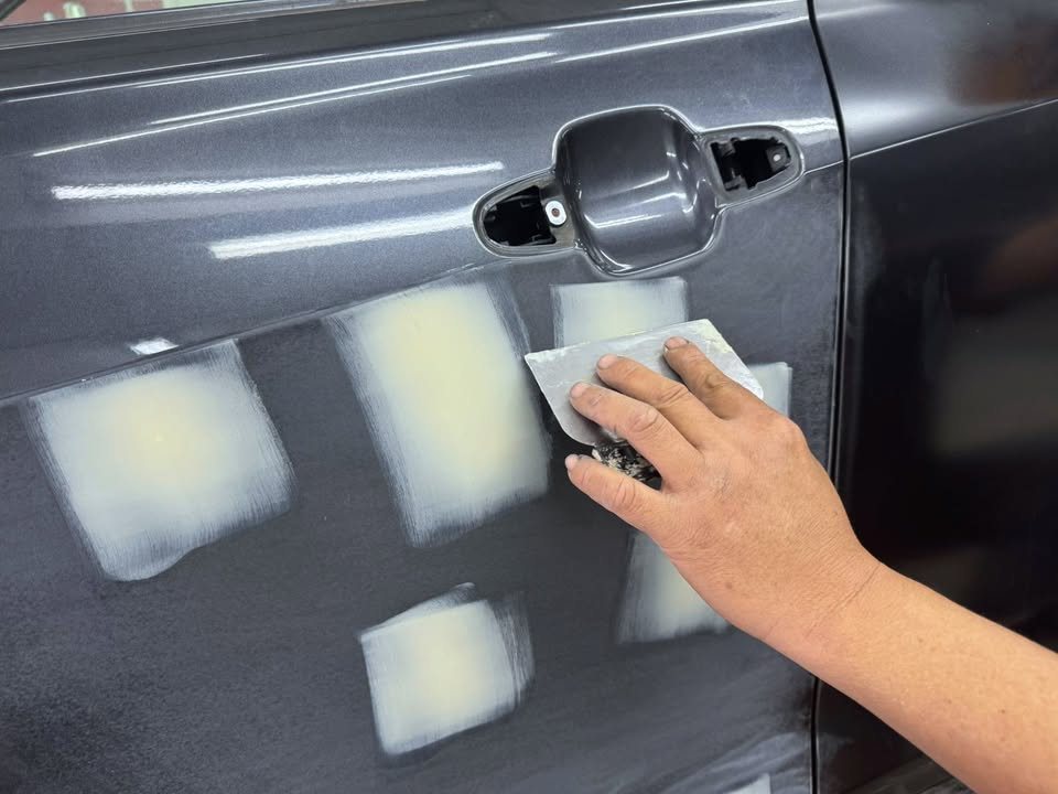 Filler patches on the Forester's door being sanded by hand.