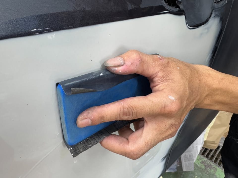 Wet sanding a primed light grey panel with a blue sanding block.