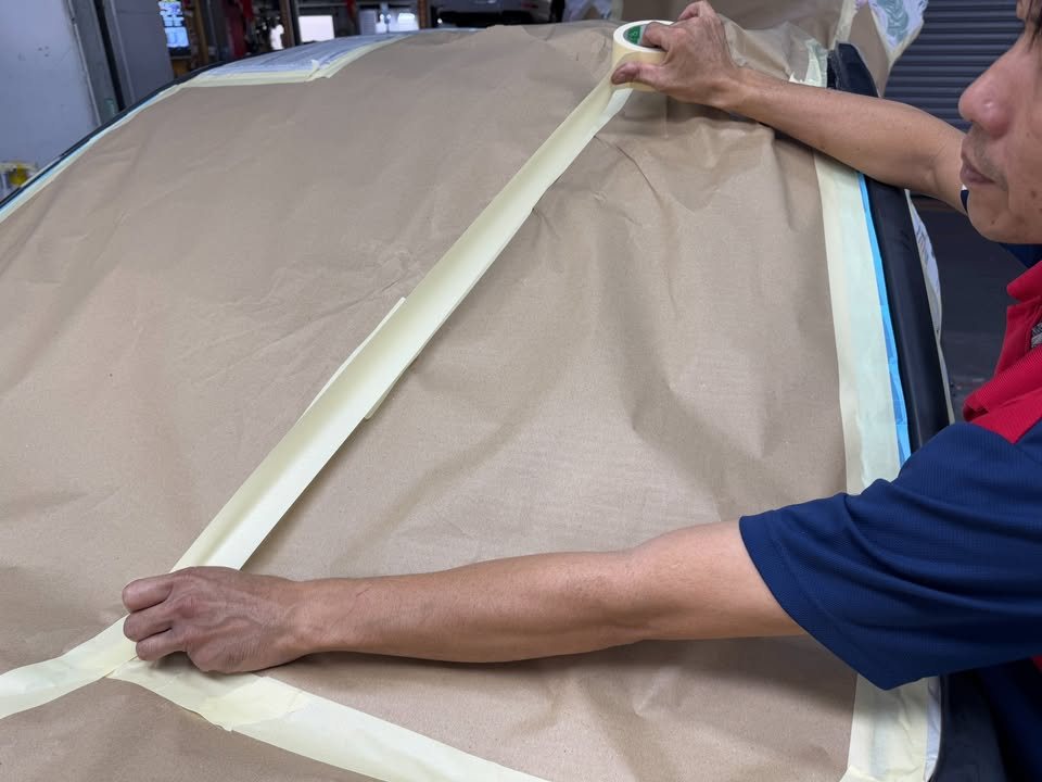 Technician masking the car with brown paper and tape.