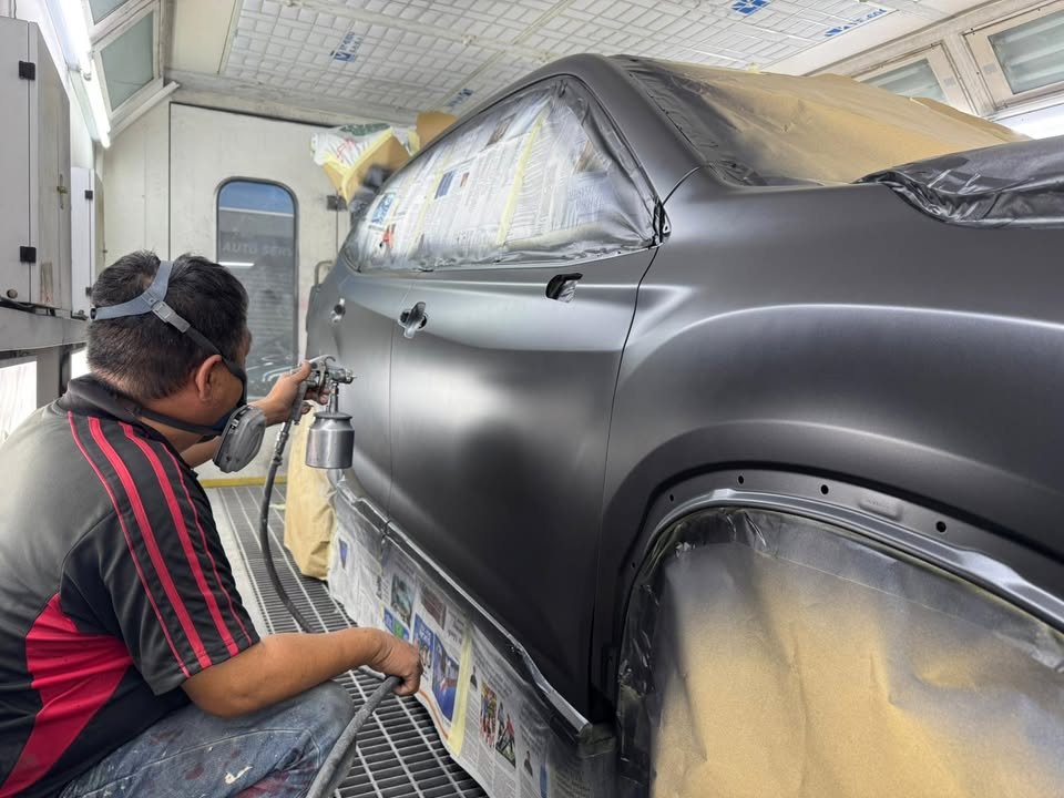Painter spraying the side of the masked Forester in the spray booth.