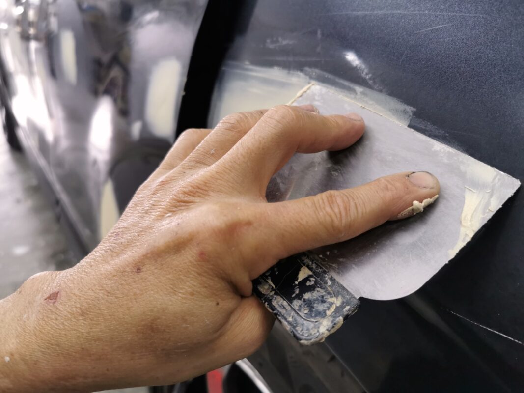 Body filler being applied to patch dents and chips on the Subaru Forester.
