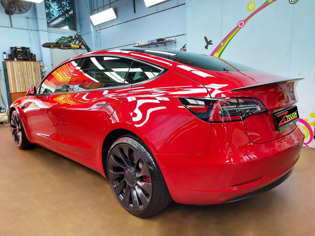 Rear quarter of the red Tesla Model 3, glossy and protected.