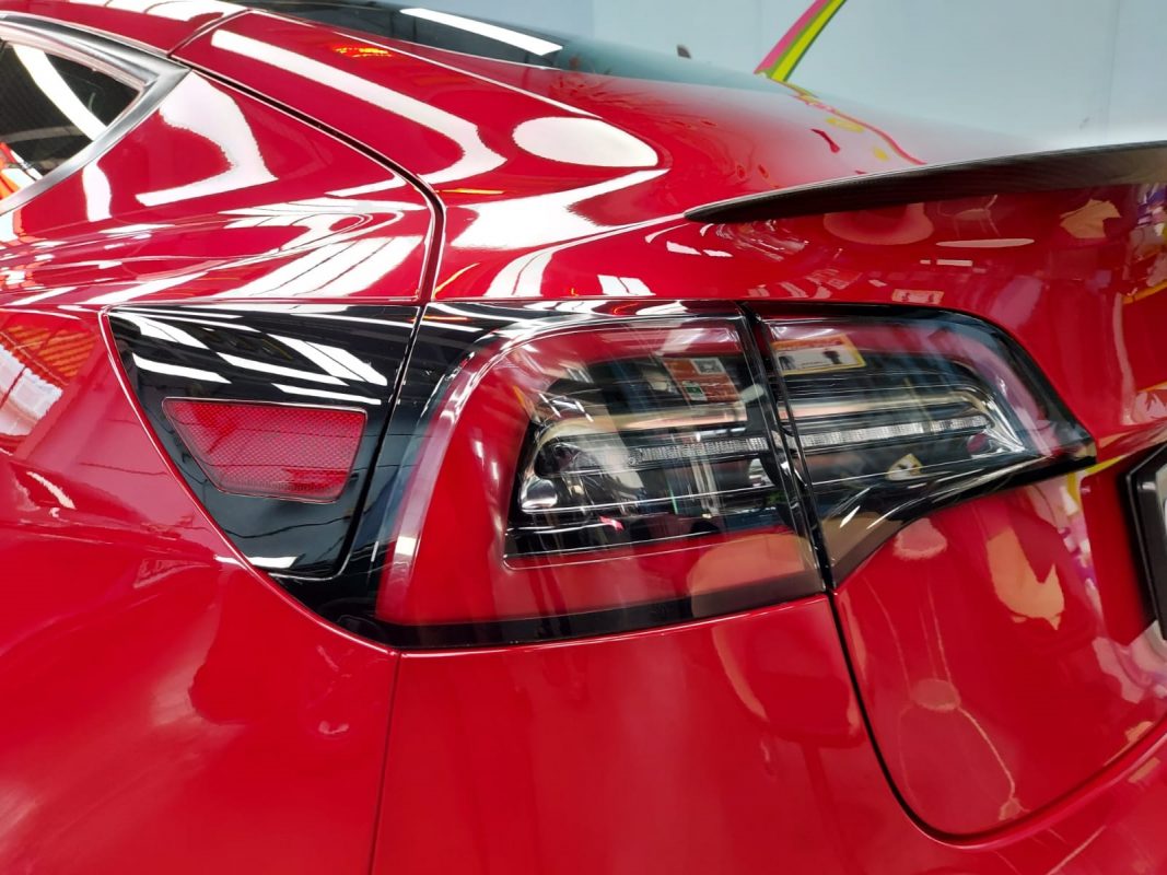 The coated bonnet of the red Tesla Model 3 under workshop lighting.