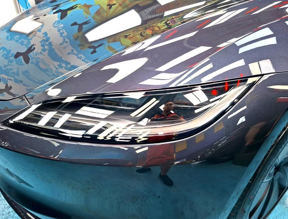 Close-up of the Model 3 headlight and bonnet edge with sharp reflections in the grey paint.