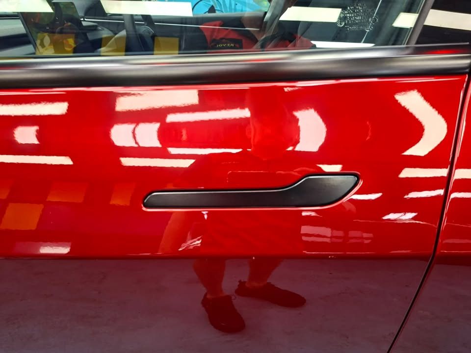 Side view of a red door with its flush black handle and reflections in the paint.