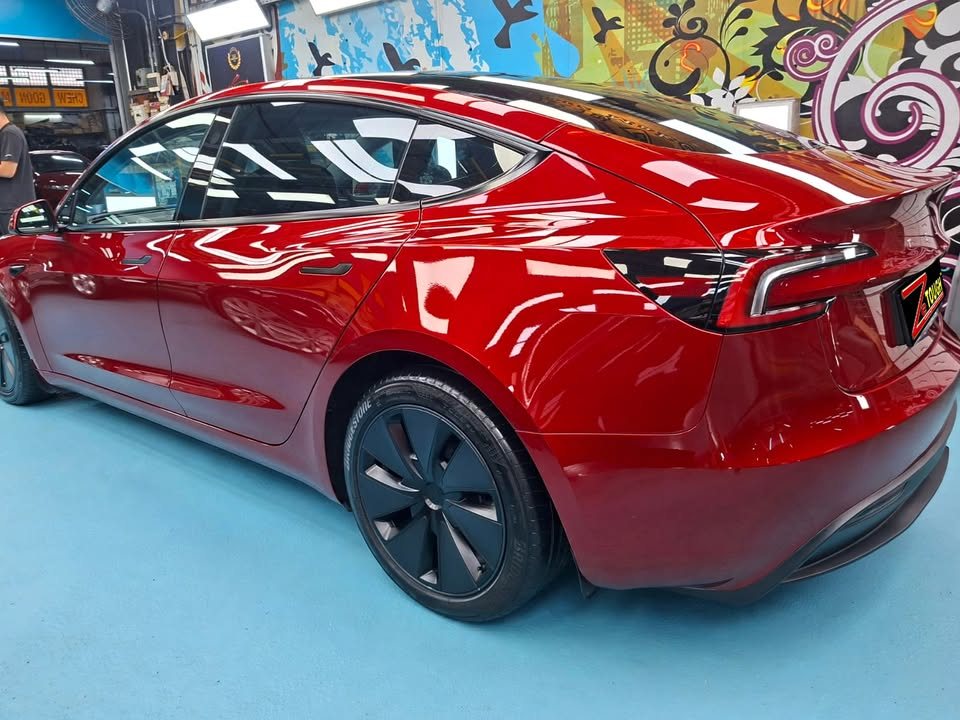 Rear three-quarter view of the red Tesla Model 3 with black wheels.