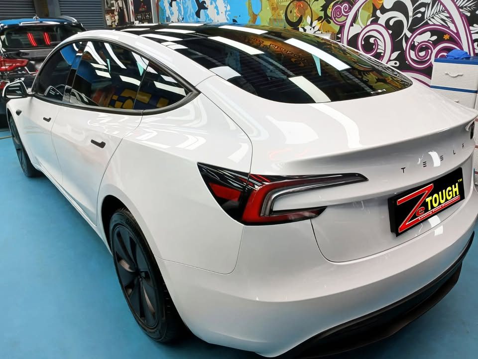 Rear three-quarter view of the white Tesla Model 3 with its black glass roof.