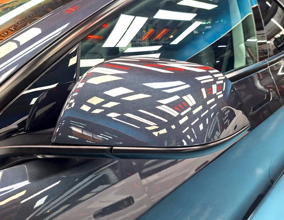 Side mirror of the Tesla reflecting the workshop ceiling lights.