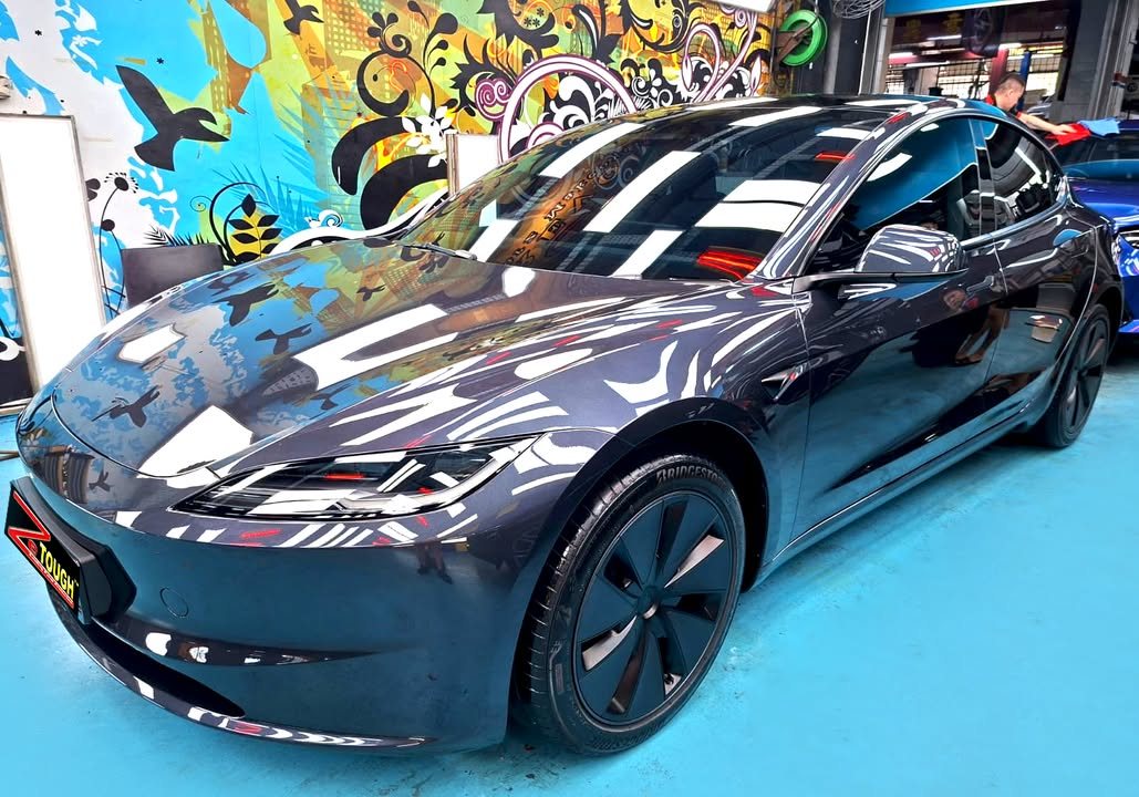 Dark grey Tesla Model 3 from the front three-quarter, its bonnet reflecting the workshop lights after the ZeTough Titanium coating.
