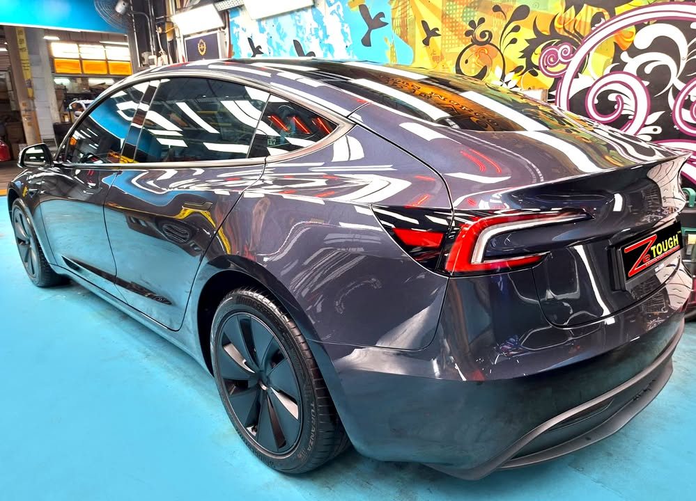 Rear three-quarter view of the dark grey Tesla Model 3 in the workshop.