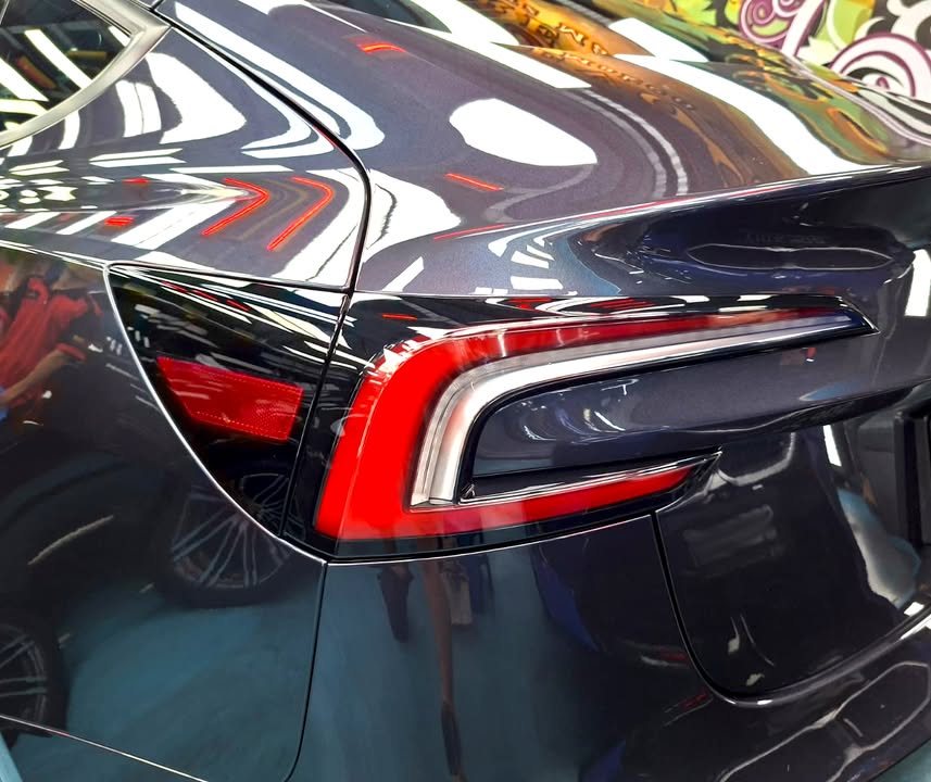 Red tail lamp on the glossy dark grey rear quarter of the Model 3.