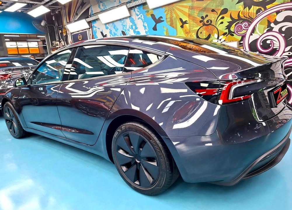 Rear three-quarter view of the dark grey Tesla Model 3 with aero wheel covers.