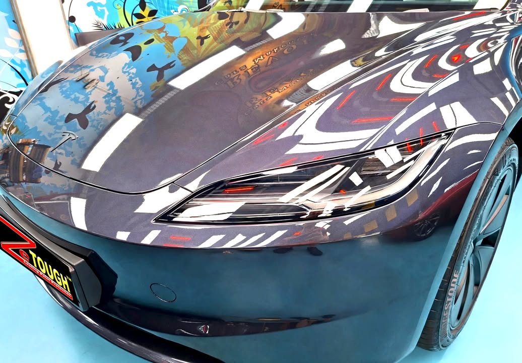 Front bumper and headlamp of the Tesla with sharp reflections across the bonnet.