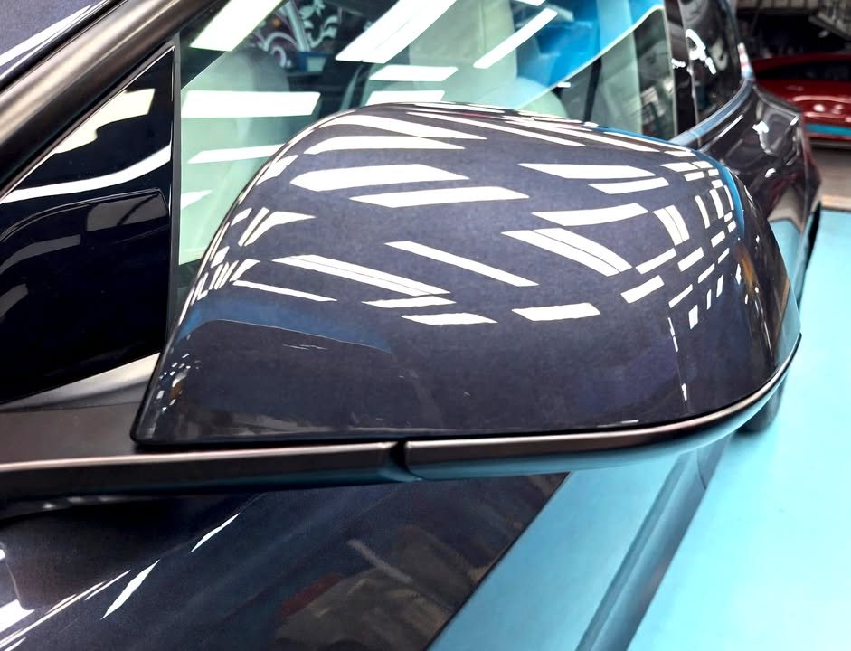 Dark grey side mirror reflecting the ceiling lights.