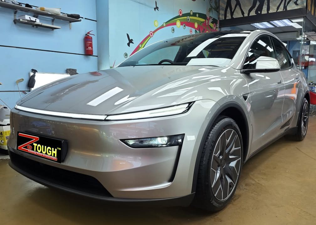 Silver Tesla Model Y L from the front three-quarter in the workshop, light bar across the nose.