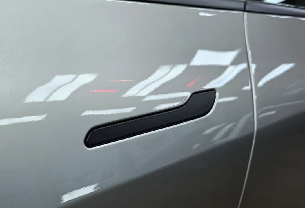 Silver door panel with a black flush handle and sharp reflections.