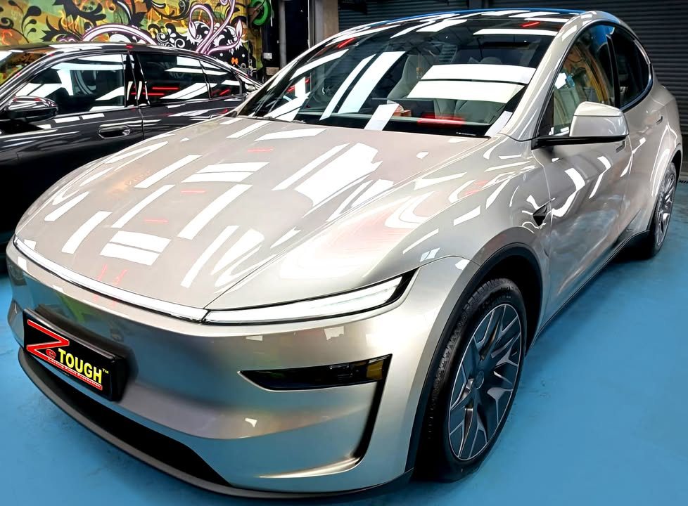 Front three-quarter view of the silver Tesla Model YL in the workshop, with its full-width front light bar.