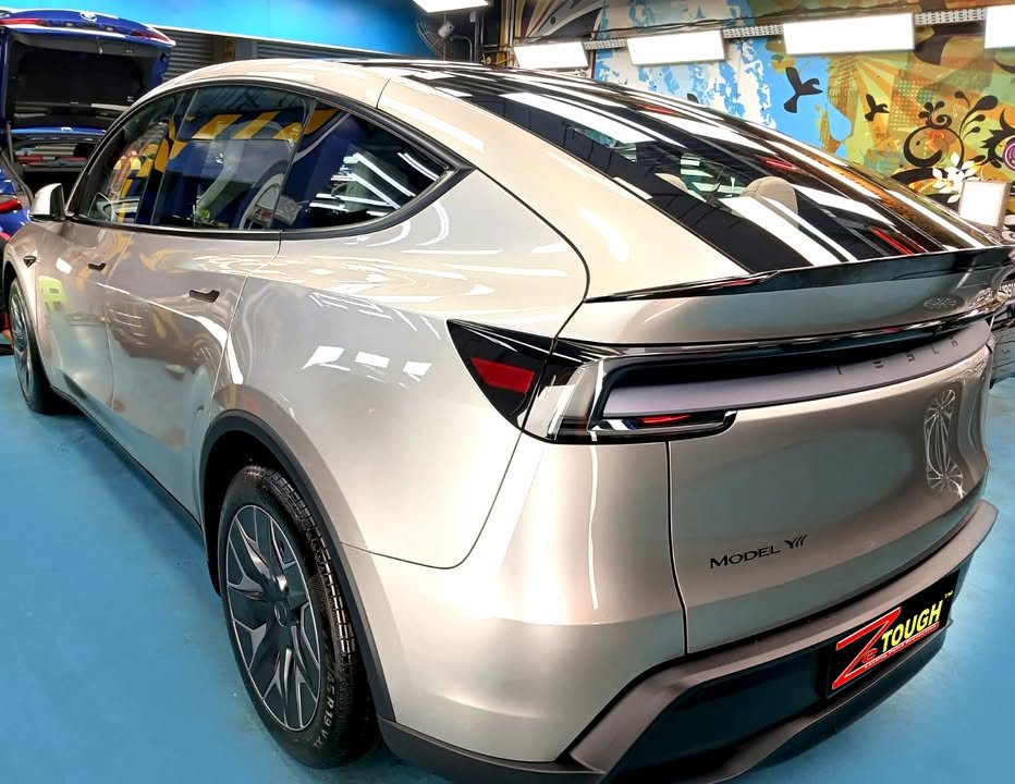 Rear three-quarter view of the silver Tesla Model YL with its full-width tail lamp.