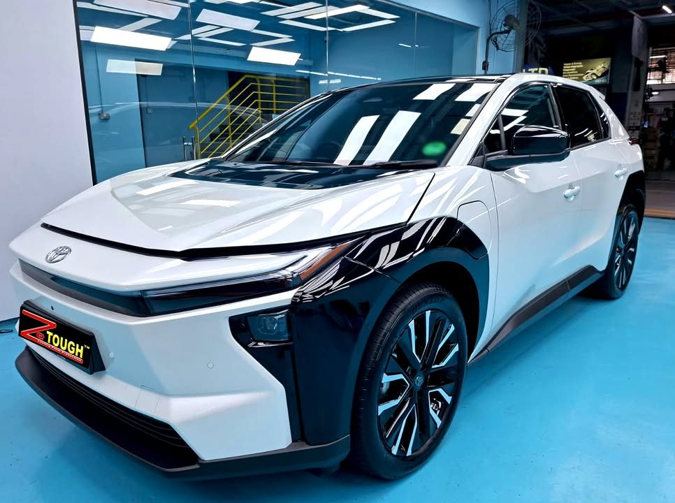 White Toyota bZ4X with black wheel arches from the front three-quarter in the Revol workshop, with a ZeTough plate on the bumper.