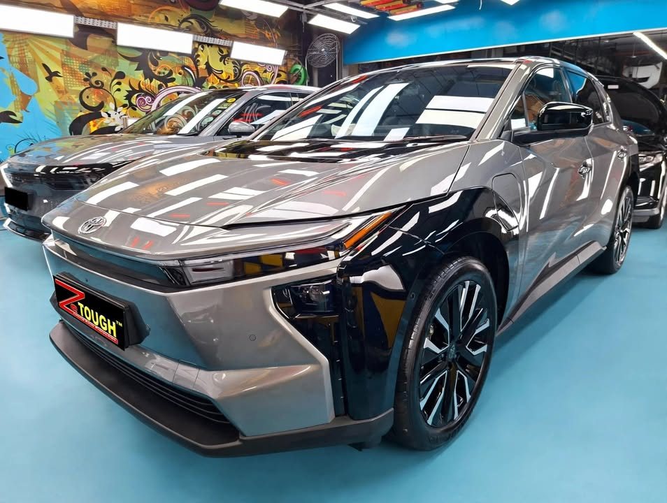 Grey Toyota bZ4X from the front three-quarter in the Revol workshop, with a ZeTough plate on the bumper.