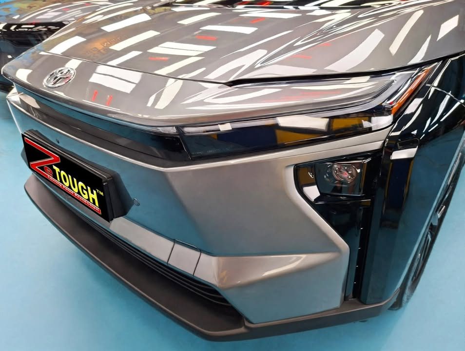 Front bumper and bonnet of the grey Toyota bZ4X with workshop lights reflected in the paint.