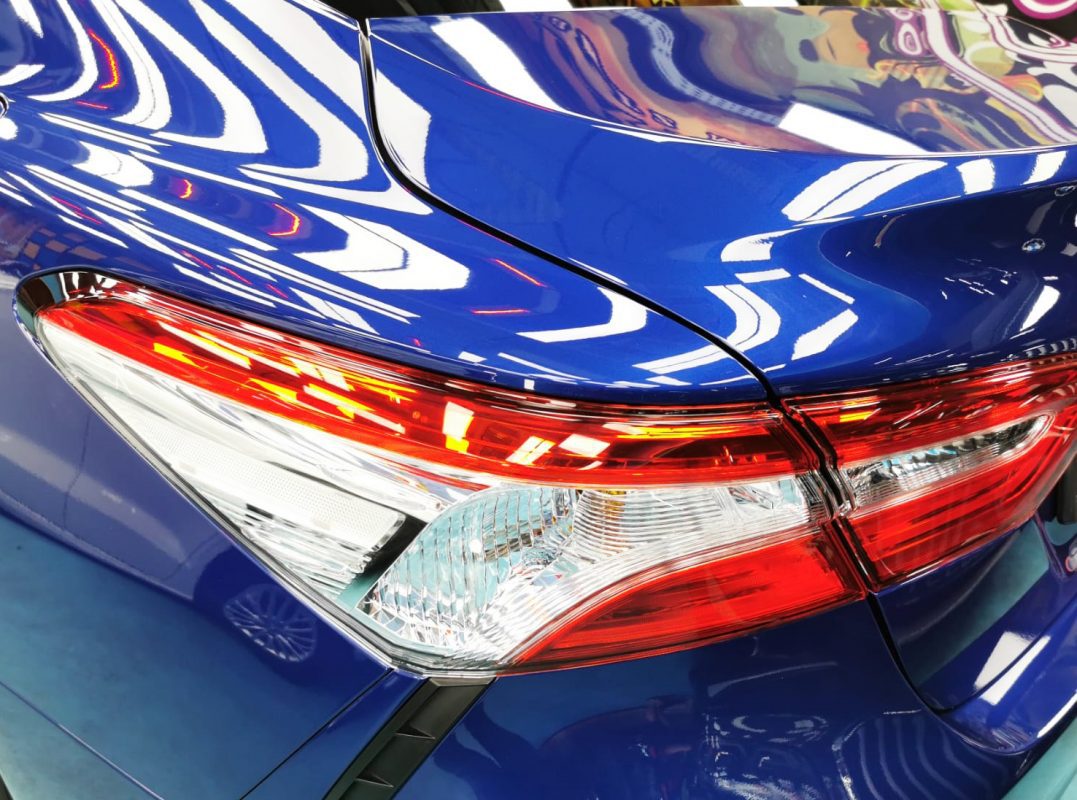 The coated bonnet of the Toyota Camry Hybrid under workshop lighting.