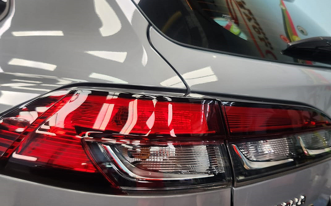 The coated bonnet of the Toyota Corolla Cross Hybrid under workshop lighting.