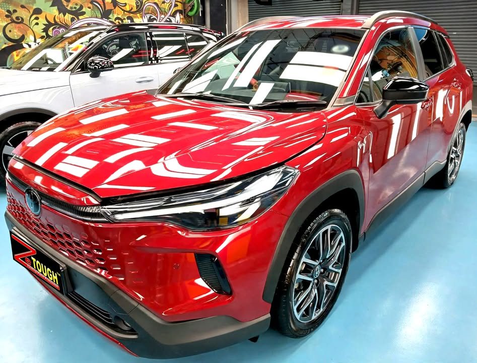 Red Toyota Corolla Cross from the front three-quarter in the Revol workshop, with a ZeTough plate on the bumper.