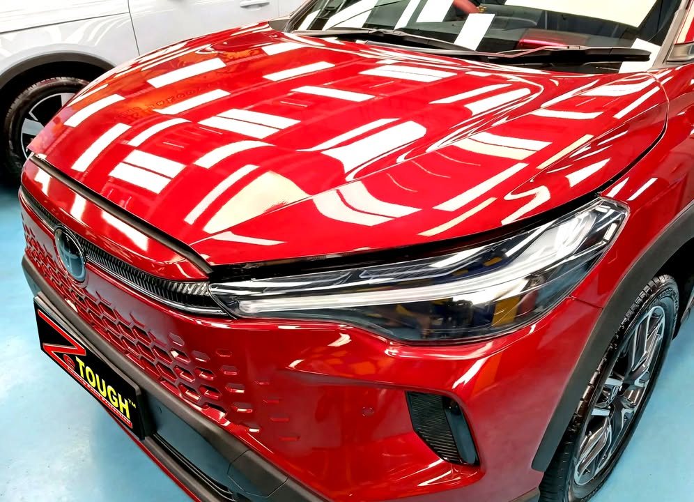Red bonnet and front grille of the Toyota with workshop lights reflected in the paint.