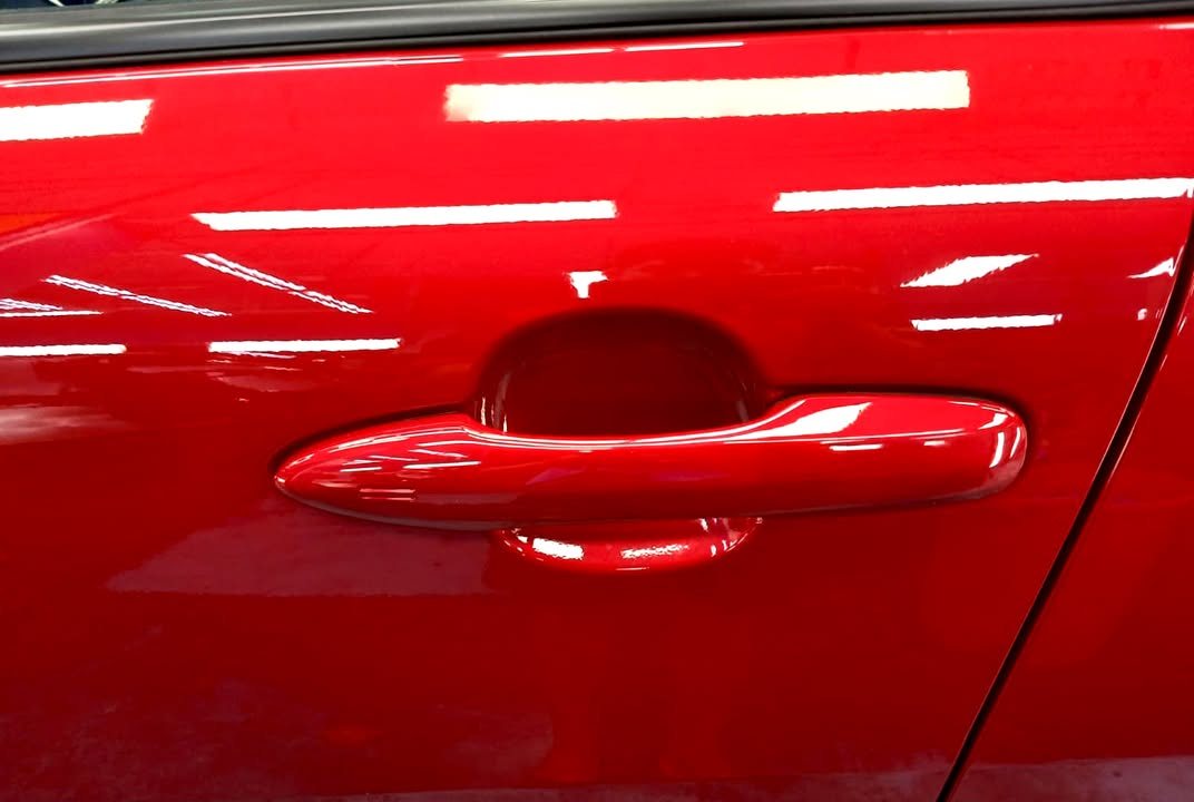 Red door handle and door panel with light reflections.