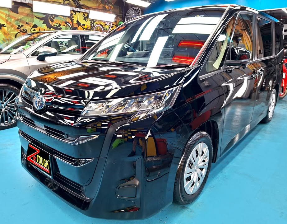 Front three-quarter view of a black Toyota Noah in the Revol Carz Makeover studio, ZeTough plate on the front bumper.