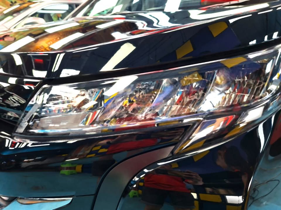 Close-up of the Toyota Noah headlight with reflections in the black bonnet.