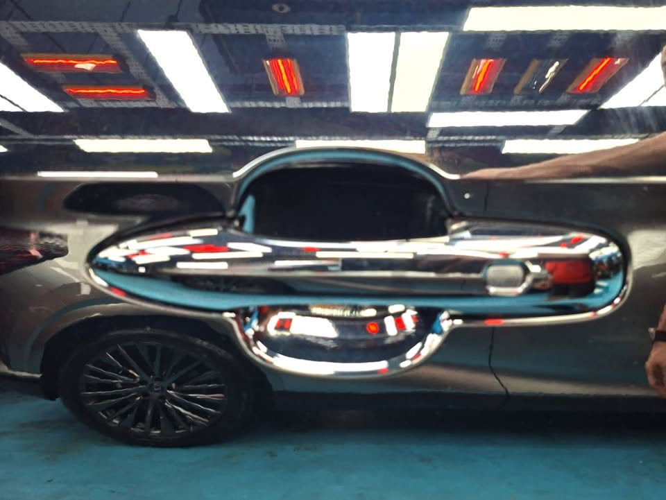 Close-up of the chrome door handle on the black Toyota Noah, reflecting the workshop.