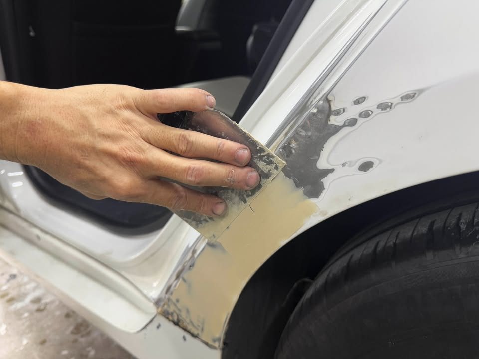 Sanding block working filler on the front wing near the wheel.
