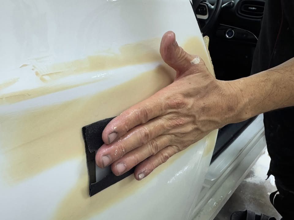 Hand sanding filler on the rear door edge.