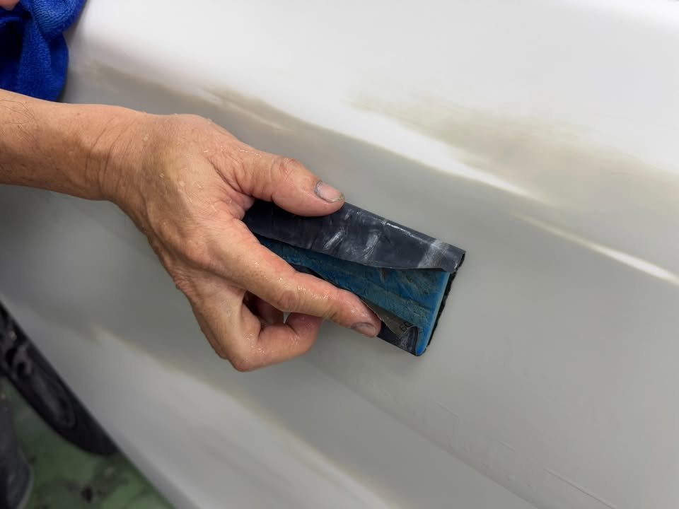 Blue sanding block on a primed patch along the side panel.